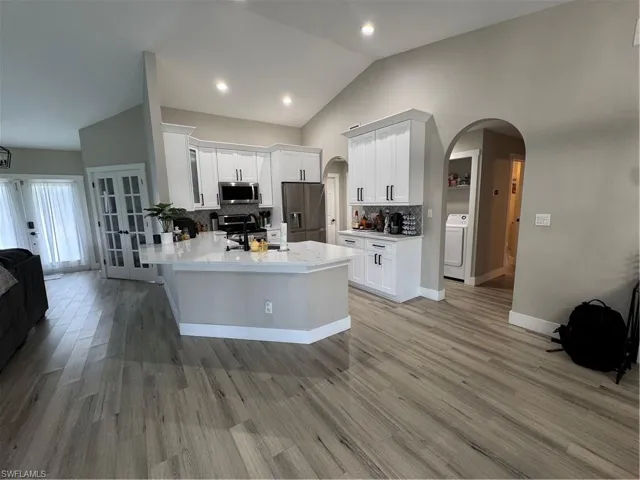 Modern kitchen featuring white cabinetry with dark hardware, stainless steel appliances, a white quartz island with a breakfast bar, and wood-finish flooring
