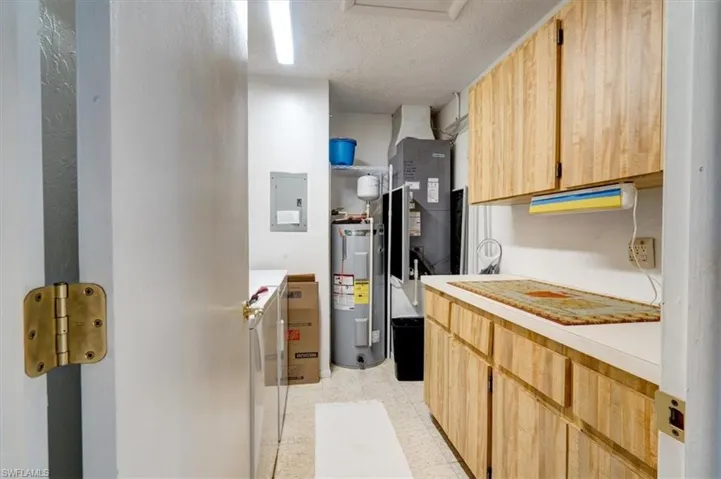 Kitchen featuring electric panel, electric water heater, light brown cabinetry, and a textured ceiling