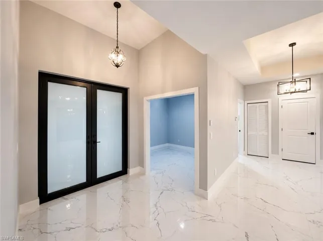 Spacious entryway featuring large format marble-look tile flooring, vaulted ceilings, and a modern chandelier