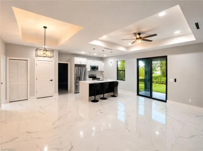 Open-concept living space with large format tile flooring and tray ceilings