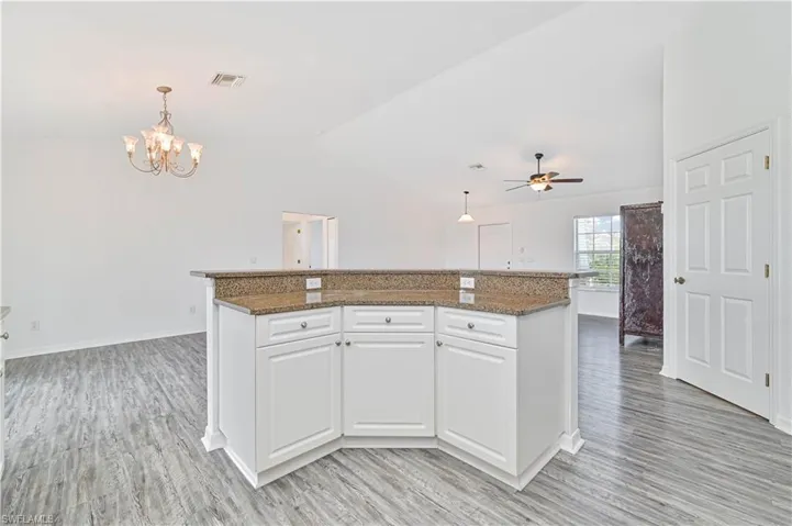 Kitchen with a center island, vaulted ceiling, decorative light fixtures, white cabinets, and light light vinyl wood-look flooring