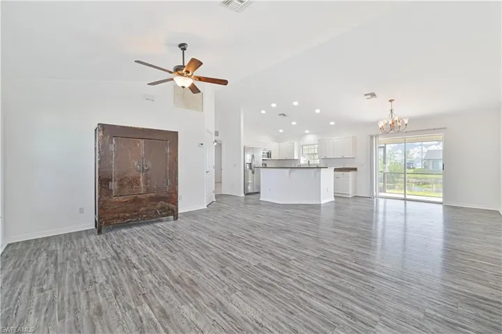 Unfurnished living room featuring cathedral ceiling, dark wood-type flooring, and ceiling fan with notable chandelier