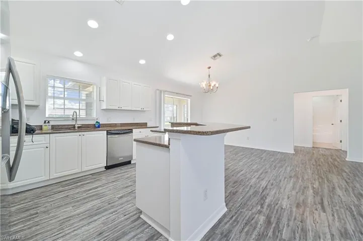 Kitchen featuring dishwasher, a kitchen island, hanging light fixtures, light light vinyl wood-look flooring and white cabinets