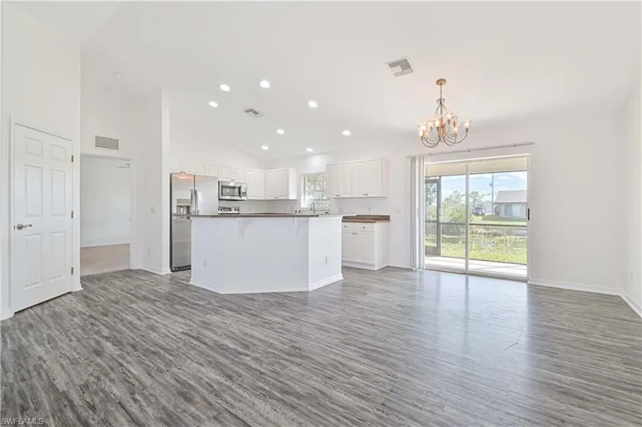 Kitchen with wood-type flooring, a kitchen island, white cabinetry, stainless steel appliances, and pendant lighting