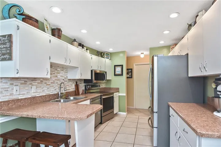 Kitchen featuring appliances with stainless steel finishes, light tile patterned floors, decorative backsplash, a peninsula, and recessed lighting