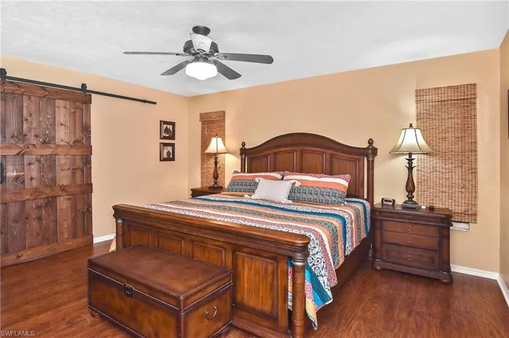 Bedroom with dark wood-type flooring, a barn door, and a ceiling fan