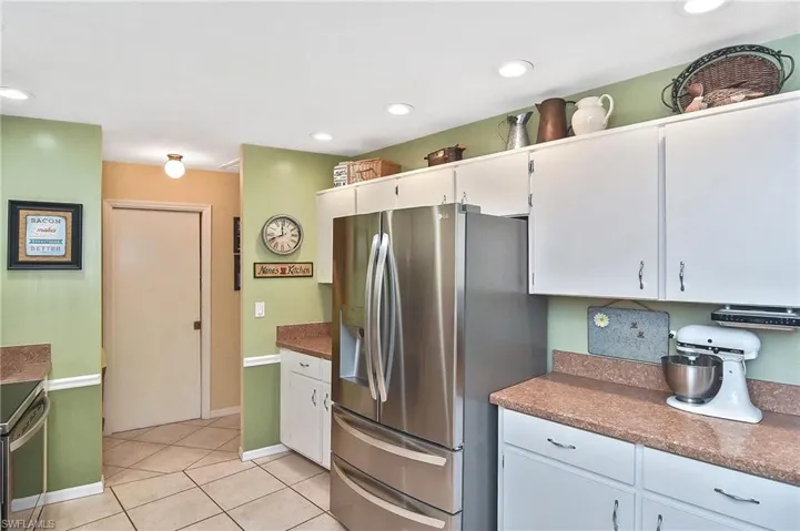 Kitchen featuring stainless steel fridge, light tile patterned flooring, white cabinets, dark countertops, and recessed lighting