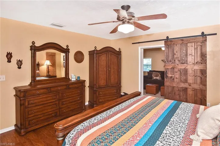 Bedroom featuring wood finished floors, a barn door, and a ceiling fan