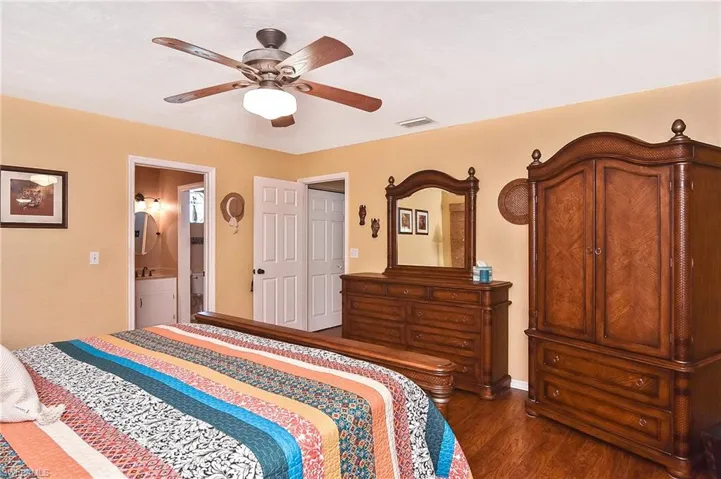 Bedroom with dark wood-style floors, ensuite bathroom, and a ceiling fan