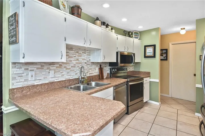 Kitchen featuring stainless steel appliances, a peninsula, decorative backsplash, white cabinets, and a kitchen breakfast bar