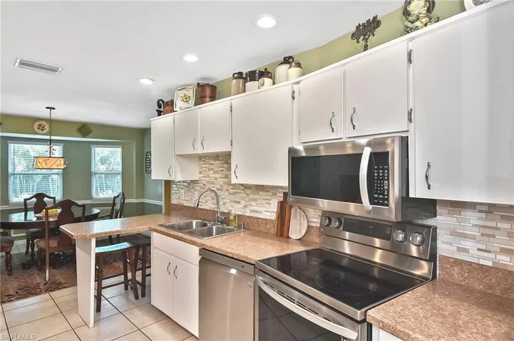 Kitchen featuring stainless steel appliances, white cabinets, light tile patterned floors, decorative backsplash, and hanging light fixtures