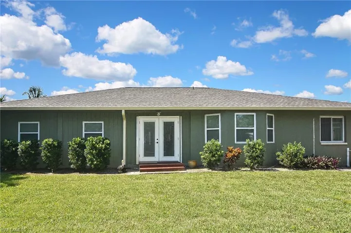 Single story home with a shingled roof, a front lawn, and french doors
