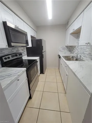 Kitchen featuring decorative backsplash, stainless steel stove, white microwave, and white cabinetry
