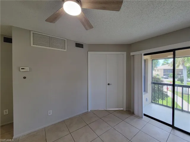 Unfurnished bedroom featuring a textured ceiling, access to outside, a closet, light tile patterned flooring, and a ceiling fan