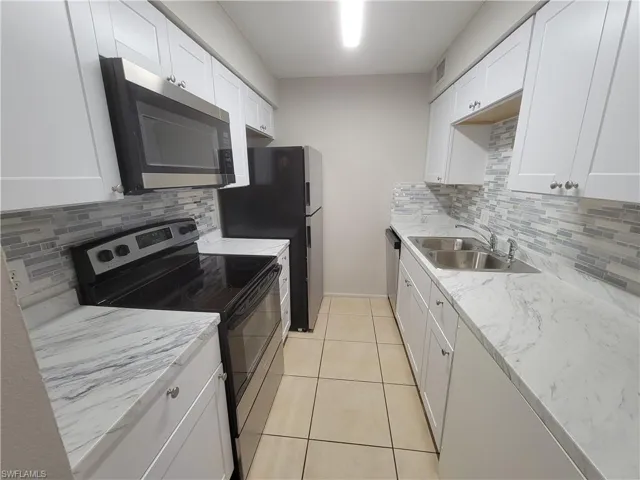 Kitchen featuring stainless steel appliances, backsplash, white cabinets, light tile patterned floors, and light stone counters