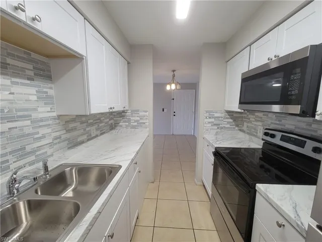 Kitchen with appliances with stainless steel finishes, white cabinets, light tile patterned flooring, pendant lighting, and decorative backsplash
