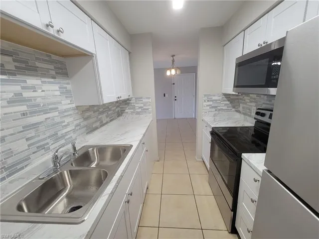 Kitchen featuring stainless steel appliances, white cabinetry, tasteful backsplash, and decorative light fixtures