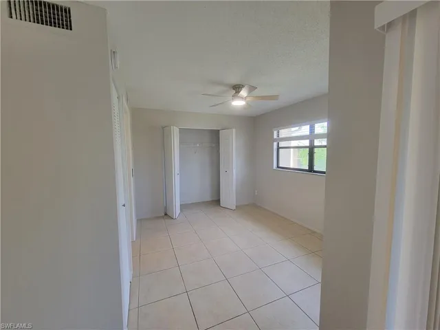 Unfurnished bedroom featuring light tile patterned flooring, a closet, a textured ceiling, and a ceiling fan