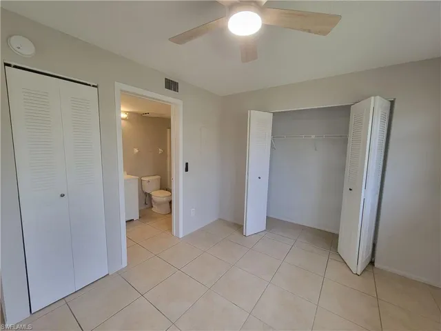 Unfurnished bedroom with light tile patterned floors, two closets, and a ceiling fan