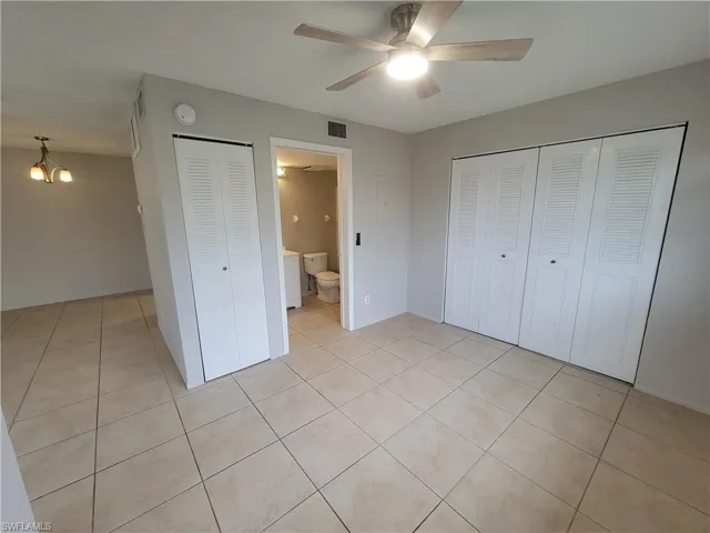 Unfurnished bedroom with light tile patterned floors, a chandelier, ceiling fan, and connected bathroom