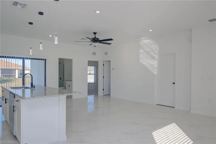 Kitchen featuring sink, white cabinetry, light stone countertops, a center island with sink, and pendant lighting