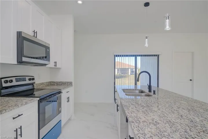 Kitchen featuring stainless steel appliances, white cabinetry, sink, and light stone counters