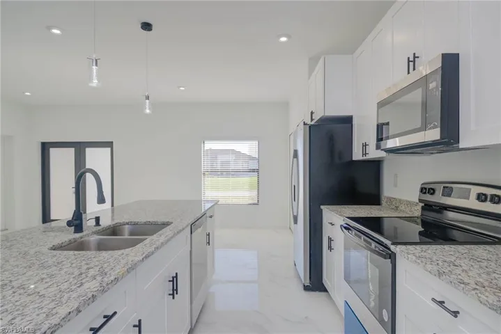 Kitchen featuring light stone countertops, pendant lighting, stainless steel appliances, white cabinets, and sink