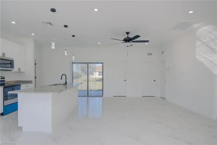 Kitchen featuring stainless steel appliances, white cabinetry, light stone counters, a center island with sink, and pendant lighting