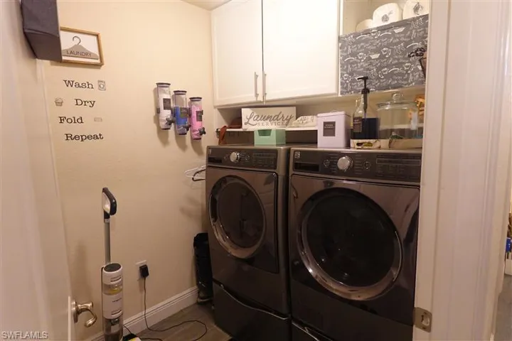 Laundry area with tile patterned flooring, washing machine and clothes dryer, and cabinets