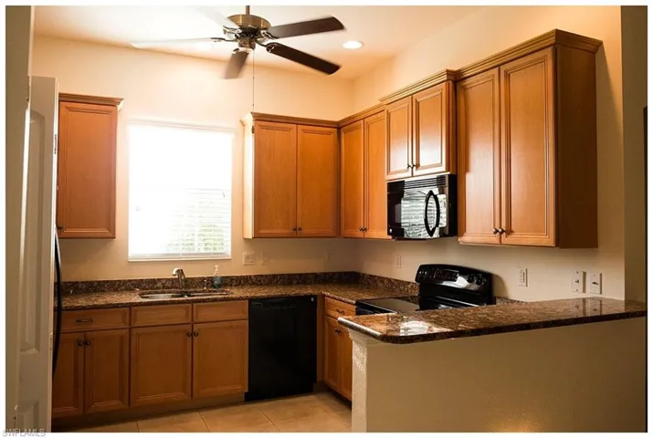 Kitchen featuring light tile patterned floors, sink, black appliances, dark stone counters, and ceiling fan