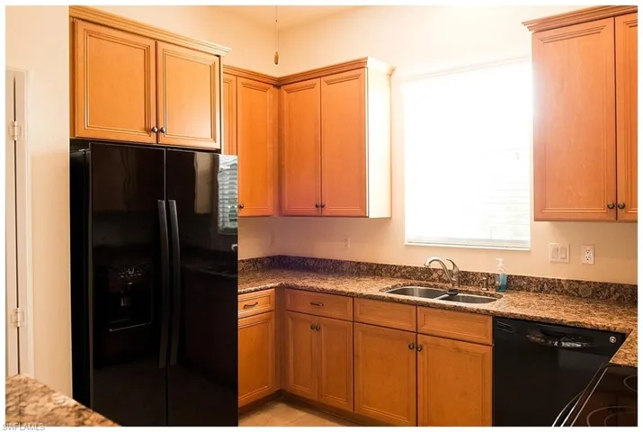 Kitchen featuring dark stone countertops, black appliances, light tile patterned floors, and sink
