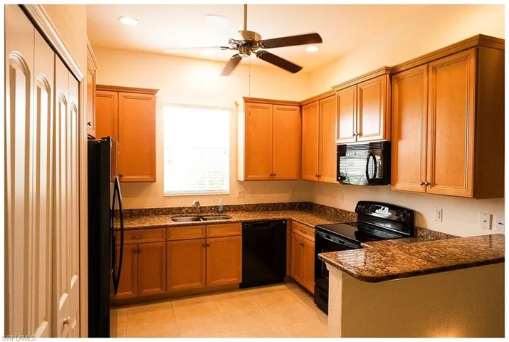 Kitchen featuring black appliances, light tile patterned floors, sink, ceiling fan, and dark stone counters