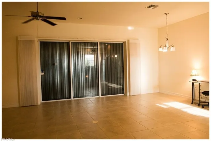 Tiled empty room featuring ceiling fan with notable chandelier