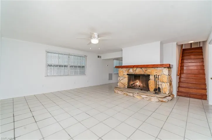Unfurnished living room with a ceiling fan, a fireplace, and stairway