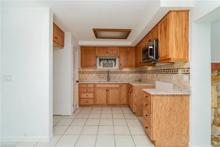 Kitchen featuring stainless steel microwave, a sink, light countertops, decorative backsplash, and light tile patterned floors