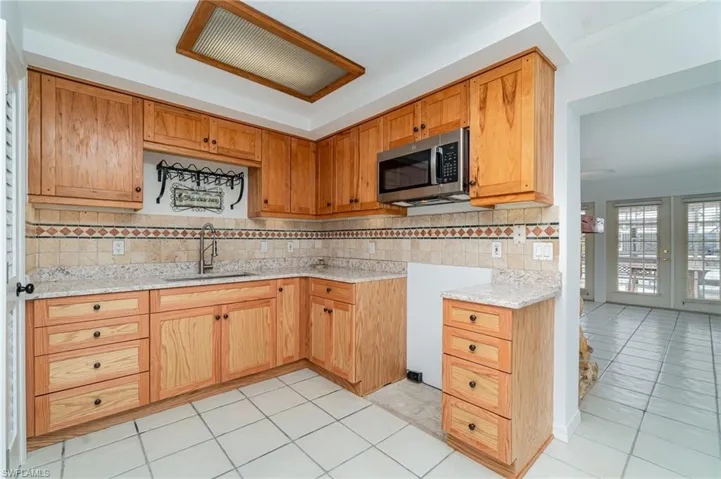 Kitchen featuring stainless steel microwave, a sink, tasteful backsplash, and light tile patterned floors