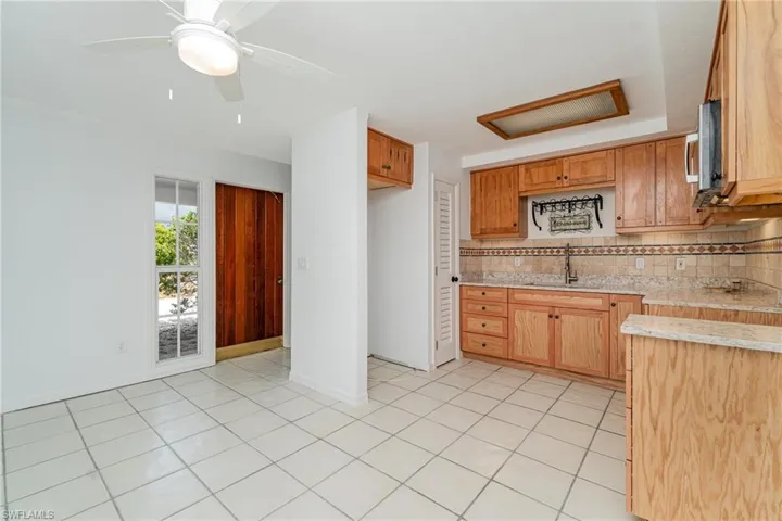Kitchen with a sink, decorative backsplash, stainless steel microwave, light tile patterned flooring, and baseboards
