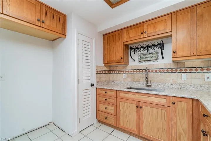 Kitchen with a sink, light tile patterned floors, light stone counters, tasteful backsplash, and brown cabinets