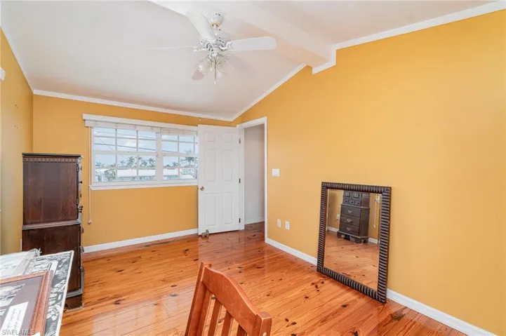 Bedroom with a wood stove, light wood-type flooring, baseboards, a ceiling fan, and ornamental molding