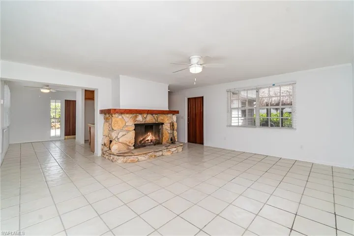 Unfurnished living room with ceiling fan, a stone fireplace, crown molding, and light tile patterned floors