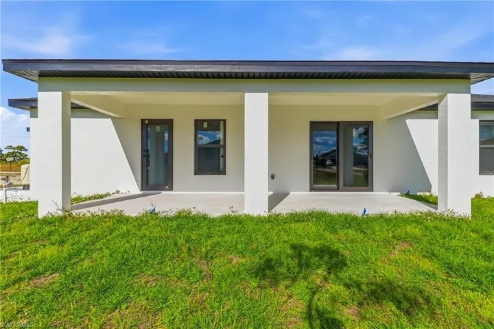 Rear view of house with stucco siding, a patio, and a lawn