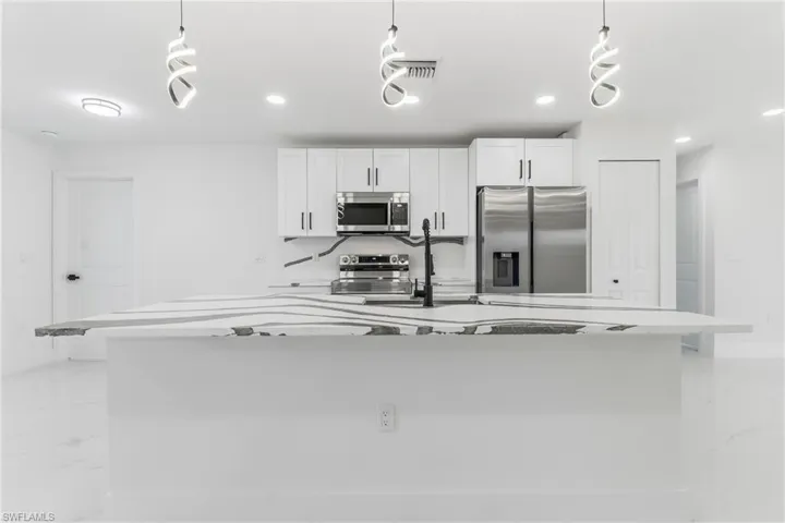 Kitchen featuring appliances with stainless steel finishes, light marble finish floors, white cabinets, recessed lighting, and a center island with sink