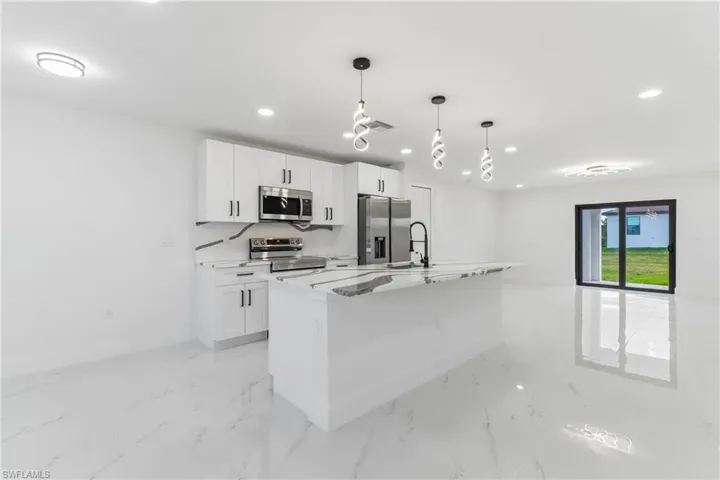 Kitchen with pendant lighting, a kitchen island with sink, white cabinetry, stainless steel appliances, and recessed lighting