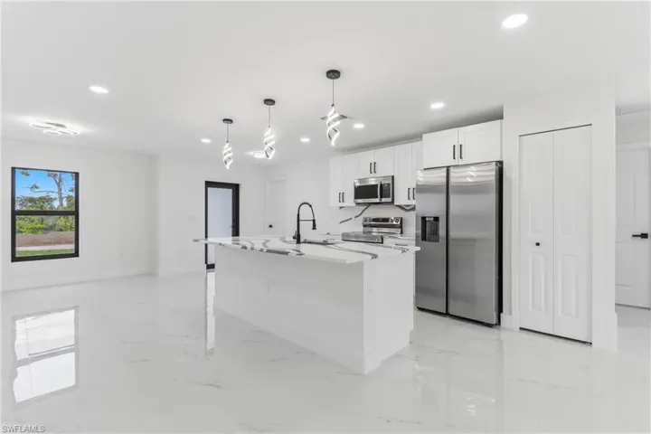 Kitchen featuring appliances with stainless steel finishes, white cabinetry, decorative light fixtures, recessed lighting, and an island with sink