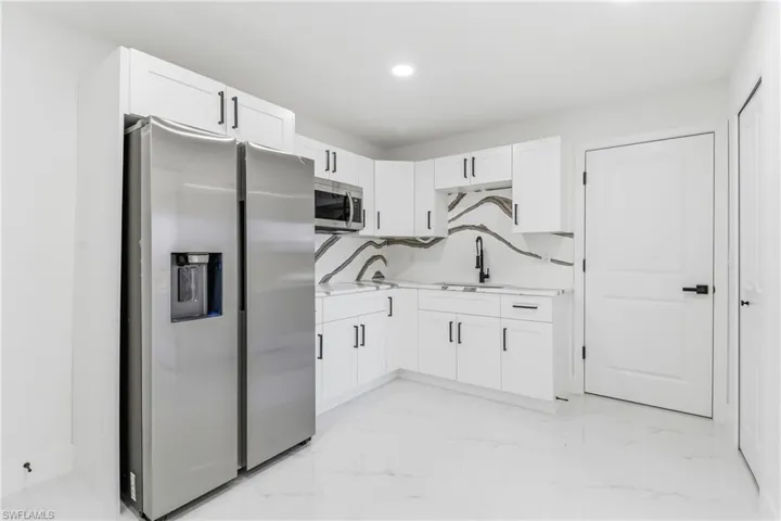 Kitchen with stainless steel appliances, light countertops, white cabinets, light marble finish flooring, and recessed lighting