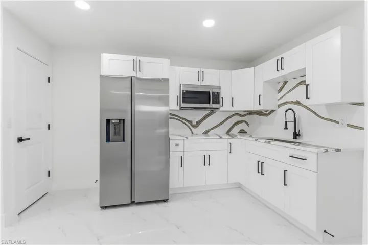 Kitchen with appliances with stainless steel finishes, white cabinets, recessed lighting, light marble finish flooring, and light stone countertops