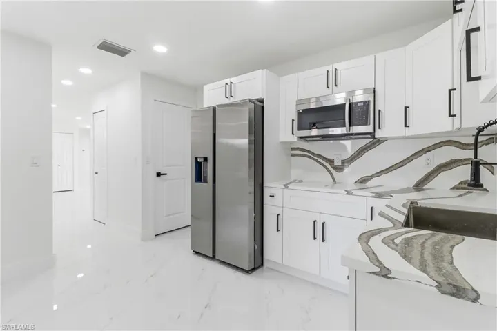 Kitchen featuring stainless steel appliances, recessed lighting, light stone counters, white cabinetry, and light marble finish floors