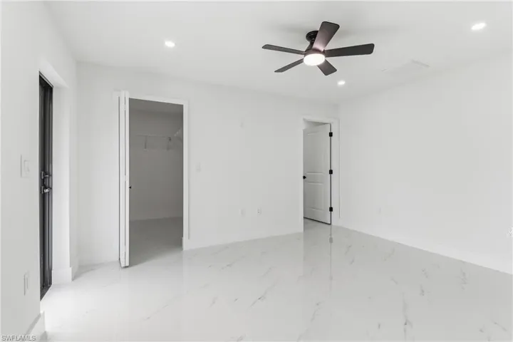 Unfurnished bedroom featuring a spacious closet, ceiling fan, light marble finish floors, and recessed lighting