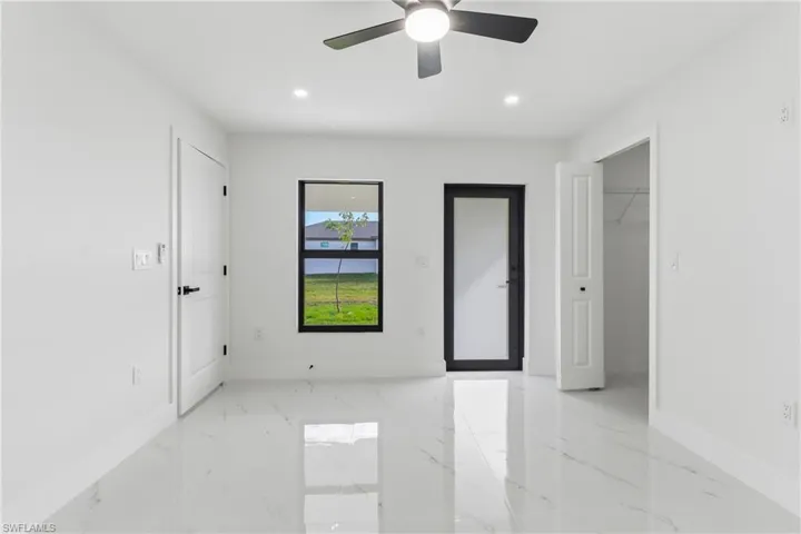 Unfurnished bedroom with a spacious closet, light marble finish flooring, ceiling fan, and recessed lighting