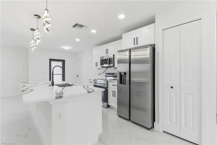 Kitchen with stainless steel appliances, pendant lighting, white cabinetry, a kitchen island with sink, and light marble finish flooring